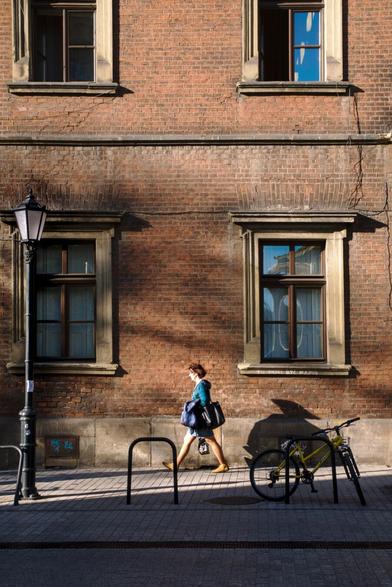 Woman walking along a red brick housefront on which the sun casts sharp shadows.