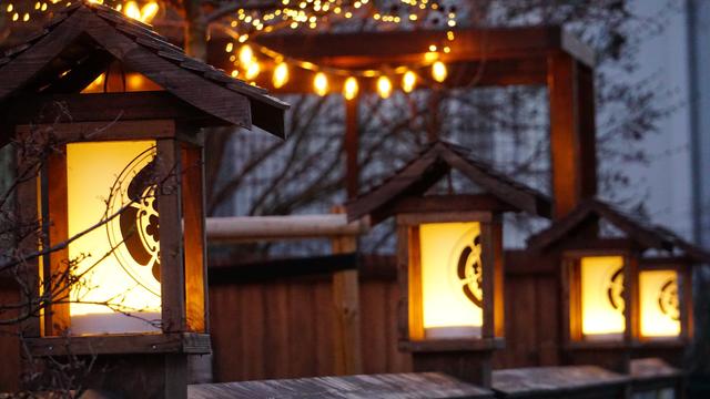 Lampions auf einem Holzzaun, darüber Lichterketten