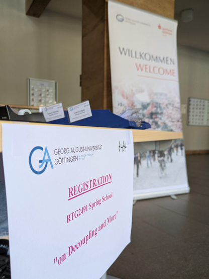 a table with a sign stating the name of the spring school, in the background a big welcome sign