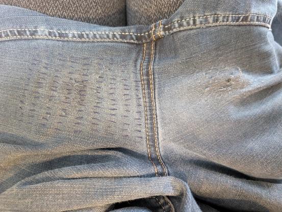 Blick auf den Schritt einer Jeans. Die linke Seite ist bereits repariert, rechts sieht man noch, wie der Original-Stoff sich langsam auflöst.