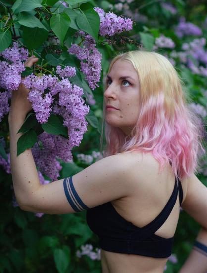 A woman with tattoos reaching for blossing lilacs