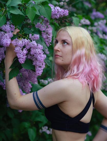 A woman with tattoos reaching for blossing lilacs