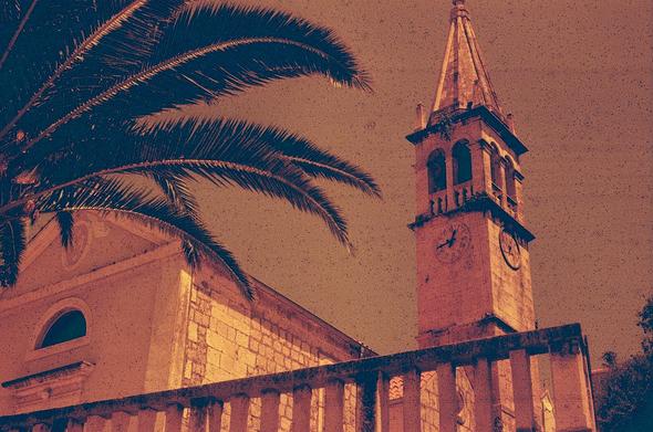 A redscale photo of a church clocktower with palm leaves in the foreground