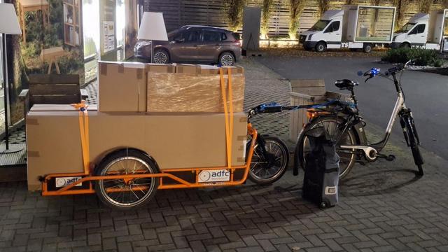 Auf dem CarlaCargo Lastenanhänger des ADFC-Münsterland sind mehrere Kartons aufgeladen, in denen die Einzelteile von 2 Kleiderschränke aus Buchenhols verpackt sind gezogen wird der Anhänger von einem Pedelec.