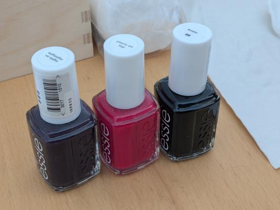 Foto von drei Essie Nagellacken, einmal (von links nach rechts) Dunkellila („sights on nightlights“), Pink („cherry in top“), und Schwarz („licorice“)