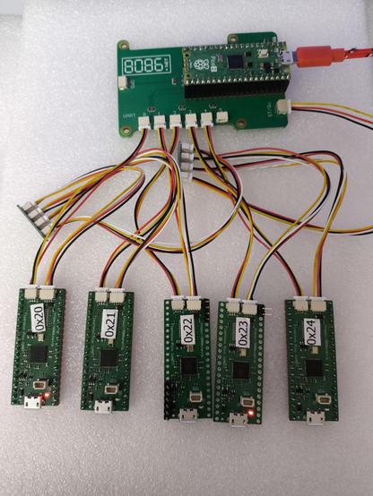 Raspberry Pi Pico2 in at the top is plugged into a green rectangular PicoUART6 PCB. At the bottom are 5 PCB similar to the Raspberry Pi Pico but with two SH connectors on the opposite end to  USB. In between is a mess of UART and I2C wires.