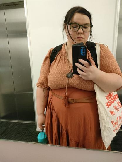 It's Robin, they're wearing a terracotta outfit that consists of a light salmon orange peasant top and a burnt orange skirt