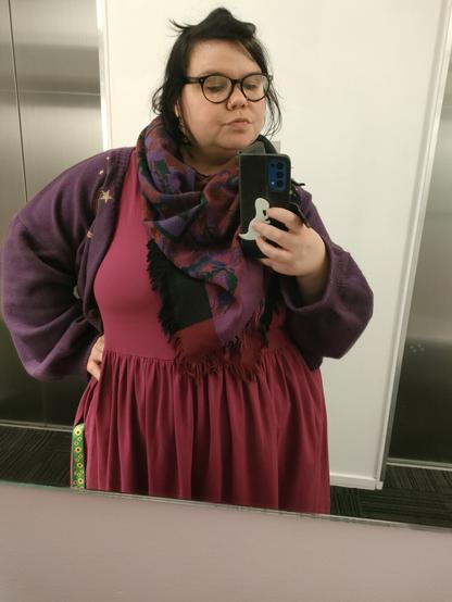 It's Robin, they're wearing a purple cardigan, a burgundy dress and a black, burgundy and purple scarf