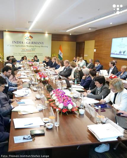 Ein langer Tisch während eines Meetings. Viele Menschen auf Deutschland und Indien beugen sich über Smartphones und Schreibblöcke und arbeiten. Im Hintergrund ein Plakat mit der Aufschrift „8th Meeting of the Indo-German Joint Working Group on Agriculture, Food Industry and Consumer Protection“.