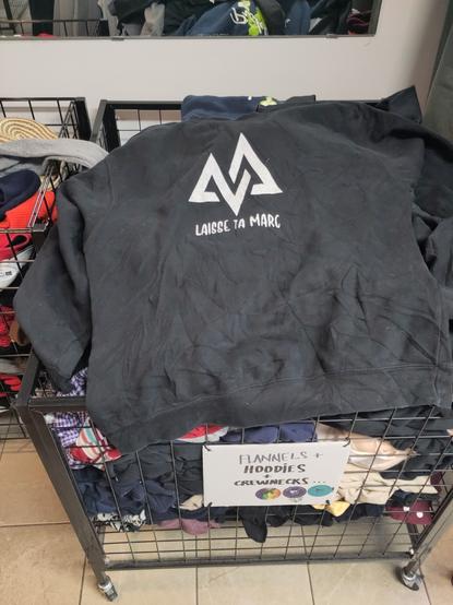 a black hoodie on a bin of hoodies with the words Laisse ta marc and a logo in white