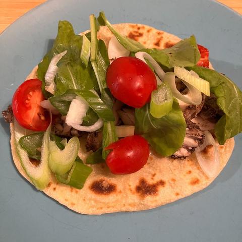 A homemade flatbread topped with chicken, greens, onion, and tomato.