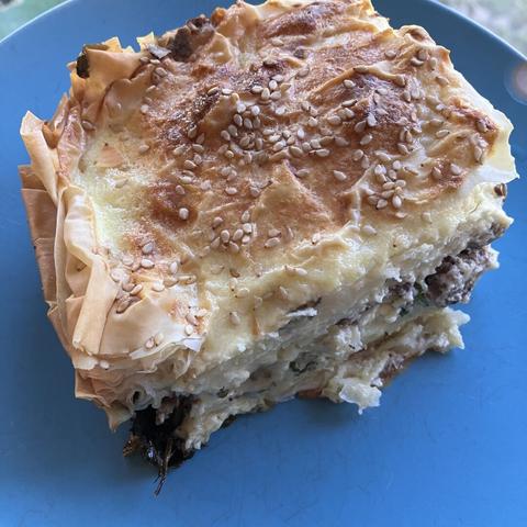 Phyllo pastry dish sprinkled with sesame seeds, with layers of meat, cheese, sauce, and spinach