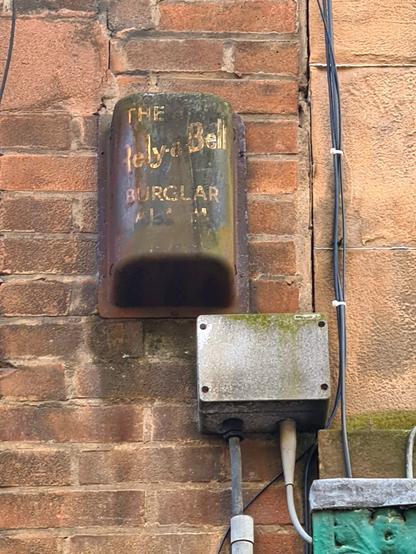 An old, rusted burglar alarm box with the text The Rely-a-Bell Burglar Alarm Company on it in gold letters.
