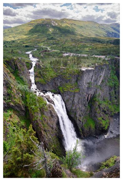 In the distance you can see a green, hilly landscape with a river meandering through it. In the foreground, the river flows into a large waterfall that cascades down a cliff.