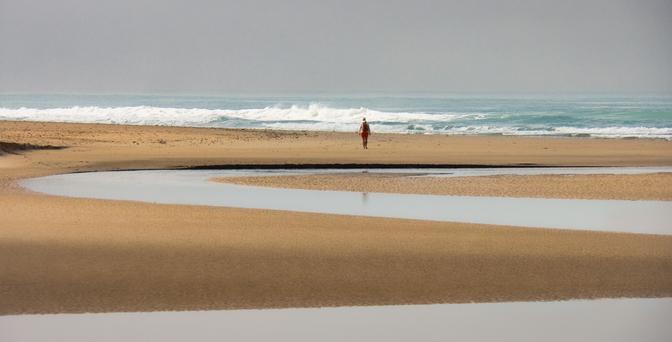dune di sabbia intervallate da lingue d'acqua, con una figura umana lontanissima, sullo sfondo.