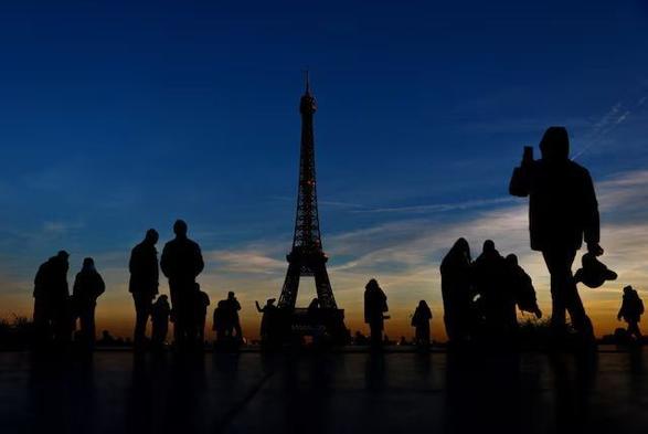 Tourists are silhouetted against the sunset as they take pictures on a cold day in Trocadero Square near the Eiffel Tower in Paris, France, January 14, 2025