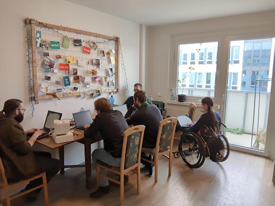 Langer Tisch in einer WG-Küche mit 5 Personen am Laptop.