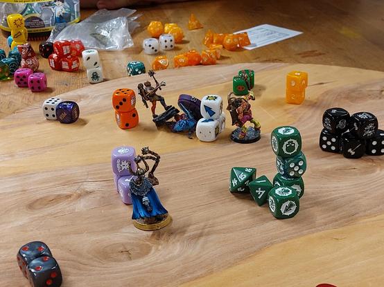 Circular game board with piles and bunches of dice acting as barriers and line of sight breakers. 4 miniatures are visible: a skaven with Punch daggers, a chaos marauder with a flail and a cape, a chaos beastman with shield and mace, and a mercenary with two maces and crossbow