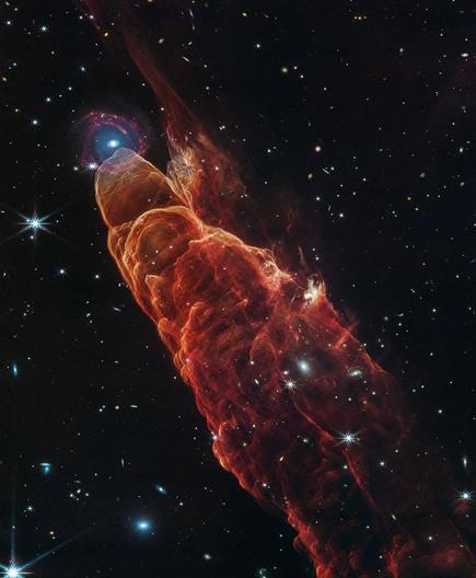 NASA’s James Webb Space Telescope observed Herbig-Haro 49/50, an outflow from a nearby still-forming star, in high-resolution near- and mid-infrared light. The intricate features of the outflow, represented in reddish-orange color, provide detailed clues about how young stars form and how their jet activity affects the environment around them. Like the wake of a speeding boat, the bow shocks in this image have an arc-like appearance as the fast-moving jet from the young star slams into the surrounding dust and gas. A chance alignment in this direction of the sky provides a beautiful juxtaposition of this nearby Herbig-Haro object with a more distant spiral galaxy in the background. Herbig-Haro 49/50 gives researchers insights into the early phases of the formation of low-mass stars similar to our own Sun. In this Webb image, blue represents light at 2.0-microns (F200W), cyan represents light at 3.3-microns (F335M), green is 4.4-microns (F444W), orange is 4.7-microns (F470N), and red is 7.7-microns (F770W). Credit: NASA, ESA, CSA, STScI