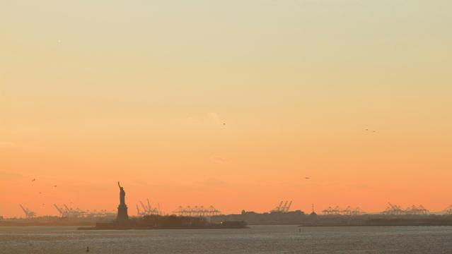 photo from 11/2022 of the statue of liberty silhouetted on an orange gradient horizon at dusk