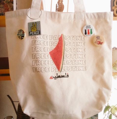 "FREE PALESTINE" の文字とスイカの絵が描かれたトートバッグに、それぞれ"SAVE GAZA" "PEACE" "Free Palestine" などと書かれた缶バッジがいくつか付いている
