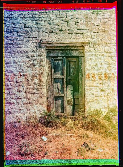 A faded painted door set in a white wall. Red handprints are painted in a line on either side. The trichrome colors are a bit distorted, and there are colorful edges where the 3 frames did not align.