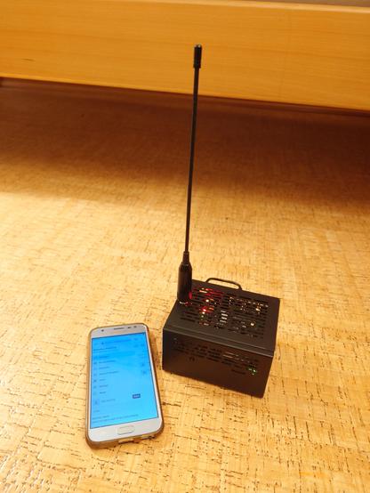 mobile phone by a case with an antenna sticking out of the top. some lights are visible in the box, which has slots in it.
