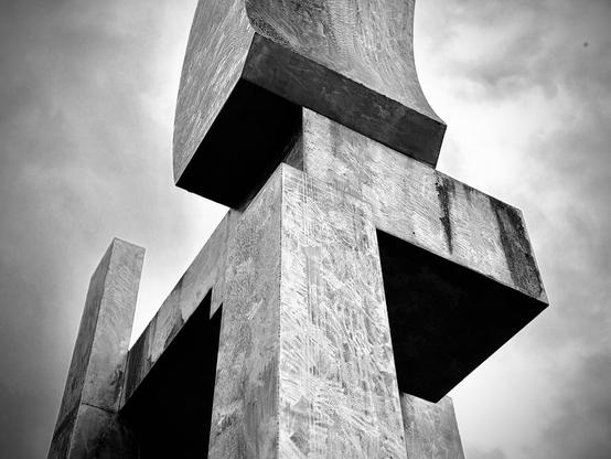 A metal art structure/sculpture with multiple rectangular, box-like pieces at different 90-degree angles (and even a curved, partial arch at the top) extends to the sky in vivid black and white.