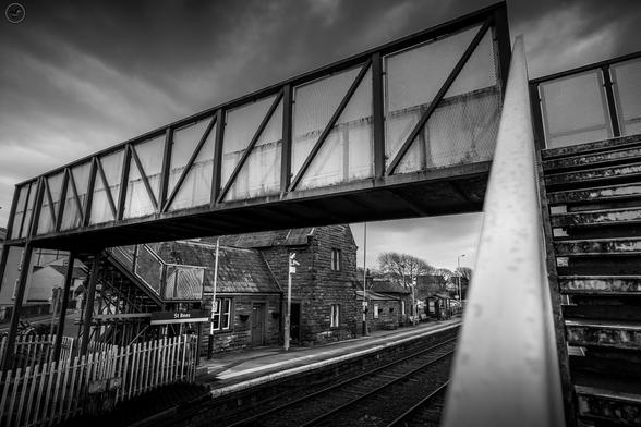 Monochrome shot of metal pedestrian bridge over railway track