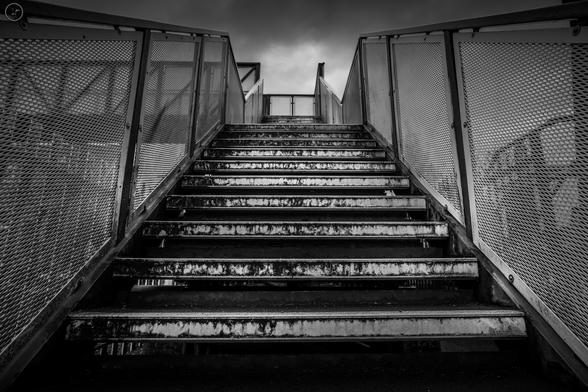 Monochrome shot of metal pedestrian bridge over railway track