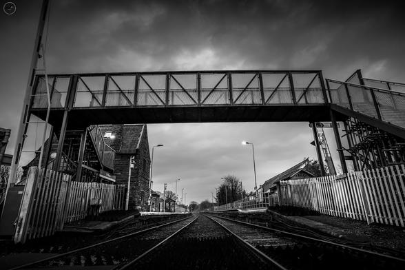 Monochrome shot of metal pedestrian bridge over railway track