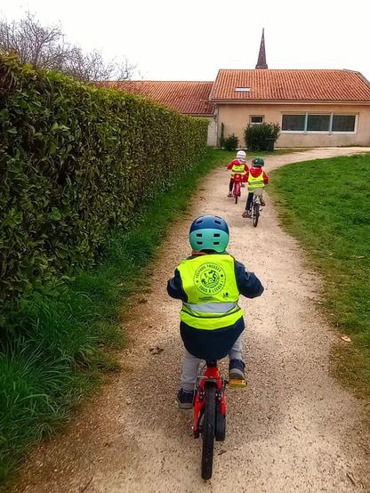 Trois enfants de 4 à 5 ans sur leur vélo respectif en chemin pour l'école maternelle de Tresses.
On peut lire le slogan "Vélobus Tresses - Tous à l'école" sur le gilet jaune d'un des enfants.