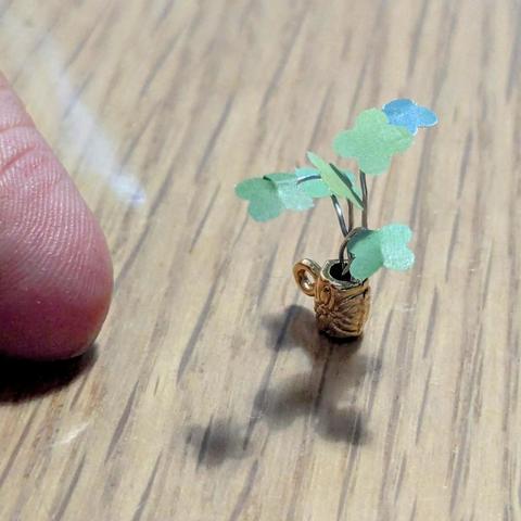 plantita montada con alambre y hojas verdes de papel, en taza o jarrón dorado, también está mi dedo para comparar el tamaño