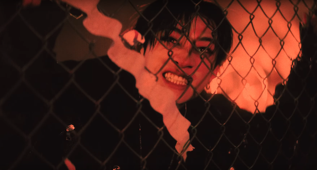 Red-lit Bang Chan looking ferocious behind a chain-link fence