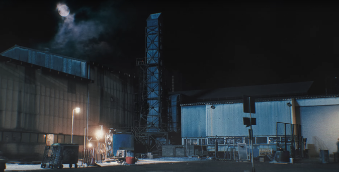 Industrial area outside at night. A blue-tinged moon is in the sky.
