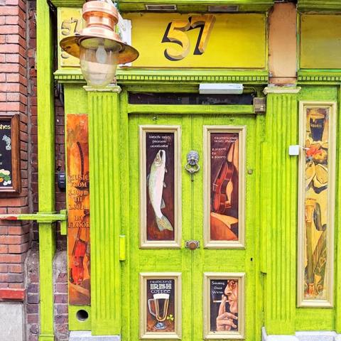 A bright green door with gold trim and a large lantern above, flanked by signs advertising lunch, dinner, music, and Irish coffee.