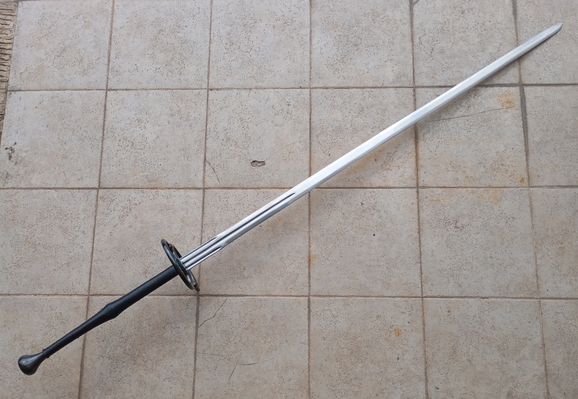 A schlachtschwert - a two-handed late medieval battle sword. The handle of the sword is wrapped in black leather and the steel of the pommel and rings are blackened.
