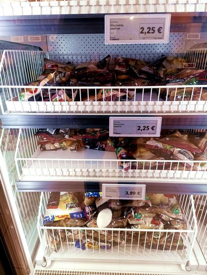 A supermarket shelf of frozen cepelinai (DE: zeppelini), filled potato dumplings that are a national food of Lithuania. One frozen potato Zeppelin has escaped its packaging and crashed like its namesake the Hindenburg onto the lowest shelf, all pale and naked like.