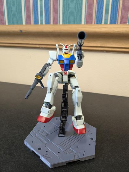 The HG RX-78-2 Revive aiming a bazooka at the viewer while on a 3D printed stand