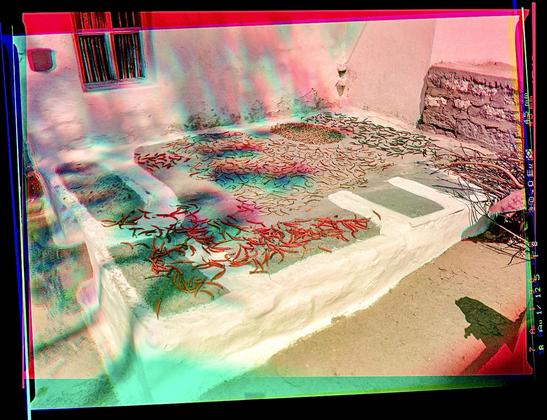 A bunch of peppers spread out on a platform in front of a building. Trichrome color shifts from moving shadows.
