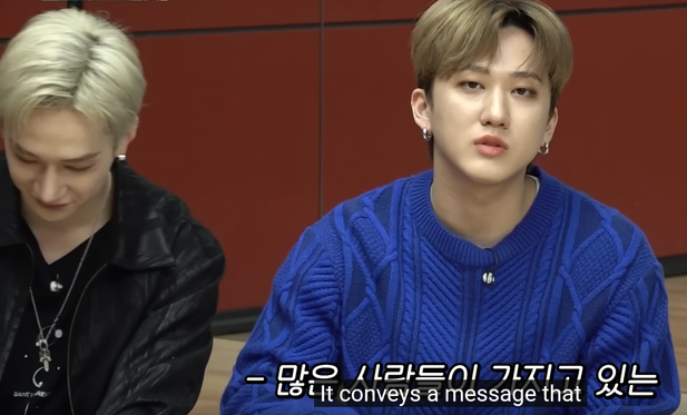 Changbin talks to the camera while Bang Chan looks down. Chan is wearing a Chrome Hearts dagger pendant on a necklace