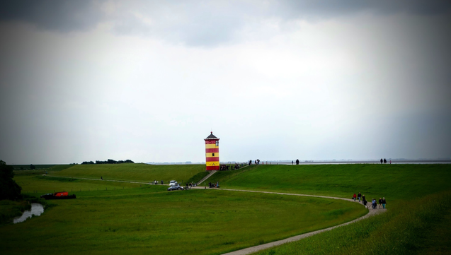 Auf einem Deich steht ein gelb-rot gestreifter Leuchturm.