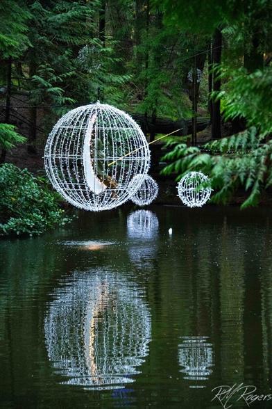 Photograph of enchanted lighted orb-structures hung above a river, reflected in the dark water below.