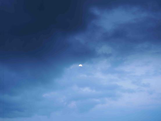 The image shows a sky with blue clouds and what appears to be a partially visible moon. The clouds have varying shades of blue, indicating it might be dusk or dawn.