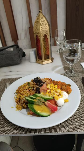 A plate containing rice, salad, moussaka and cheese, before an ornate lantern.