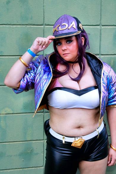 Cosplayer dressed as the character Akali, from the virtual band K/DA, produced by Riot Music/Games. The character wears a cap, top, asymmetrical pants, a holographic purple jacket and accessories.

All the clothes, with the exception of the pants, which are black, are in shades of purple and gold.