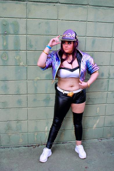Cosplayer dressed as the character Akali, from the virtual band K/DA, produced by Riot Music/Games. The character wears a cap, top, asymmetrical pants, a holographic purple jacket and accessories.

All the clothes, with the exception of the pants, which are black, are in shades of purple and gold.