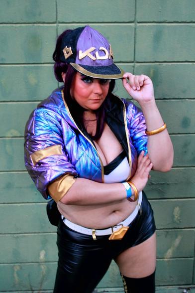 Cosplayer dressed as the character Akali, from the virtual band K/DA, produced by Riot Music/Games. The character wears a cap, top, asymmetrical pants, a holographic purple jacket and accessories.

All the clothes, with the exception of the pants, which are black, are in shades of purple and gold.
