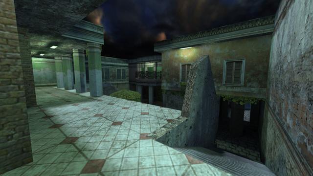 In this picture you can see from the upper floor of a building in a courtyard. To the right is a staircase that leads down to the street. The wall of the stairwell is broken. In the middle of the courtyard is a single but large hedge. On the left is an open corridor which has a roof and this is held by four columns. The corridor is lit by two white-lit lamps attached to the ceiling. Opposite this corridor is a balcony, with a dark metal railing. The balcony is also illuminated. A little further to the right, above a window closed with shutters, is another lamp. This is on the map cs_havana in the game Counter-Strike 1.6.