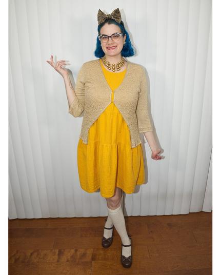 The image features a woman standing against a white curtain backdrop, wearing a vibrant yellow dress that falls just above her knees. Over the dress, she has layered a beige cardigan, adding a touch of elegance to her overall look.

On her head, she sports a cat ear headband in leopard print, complete with black ears and a gold bow at the top. Her dark hair is styled neatly, complementing the playful yet sophisticated ensemble.

The woman's outfit is completed by white knee-high socks and black Mary Jane shoes, which add a touch of whimsy to her overall appearance. The background of the image is a crisp white curtain, providing a clean and neutral contrast to the woman's bold and colorful attire.
